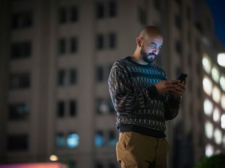 Person standing outdoors in the evening, checking their phone