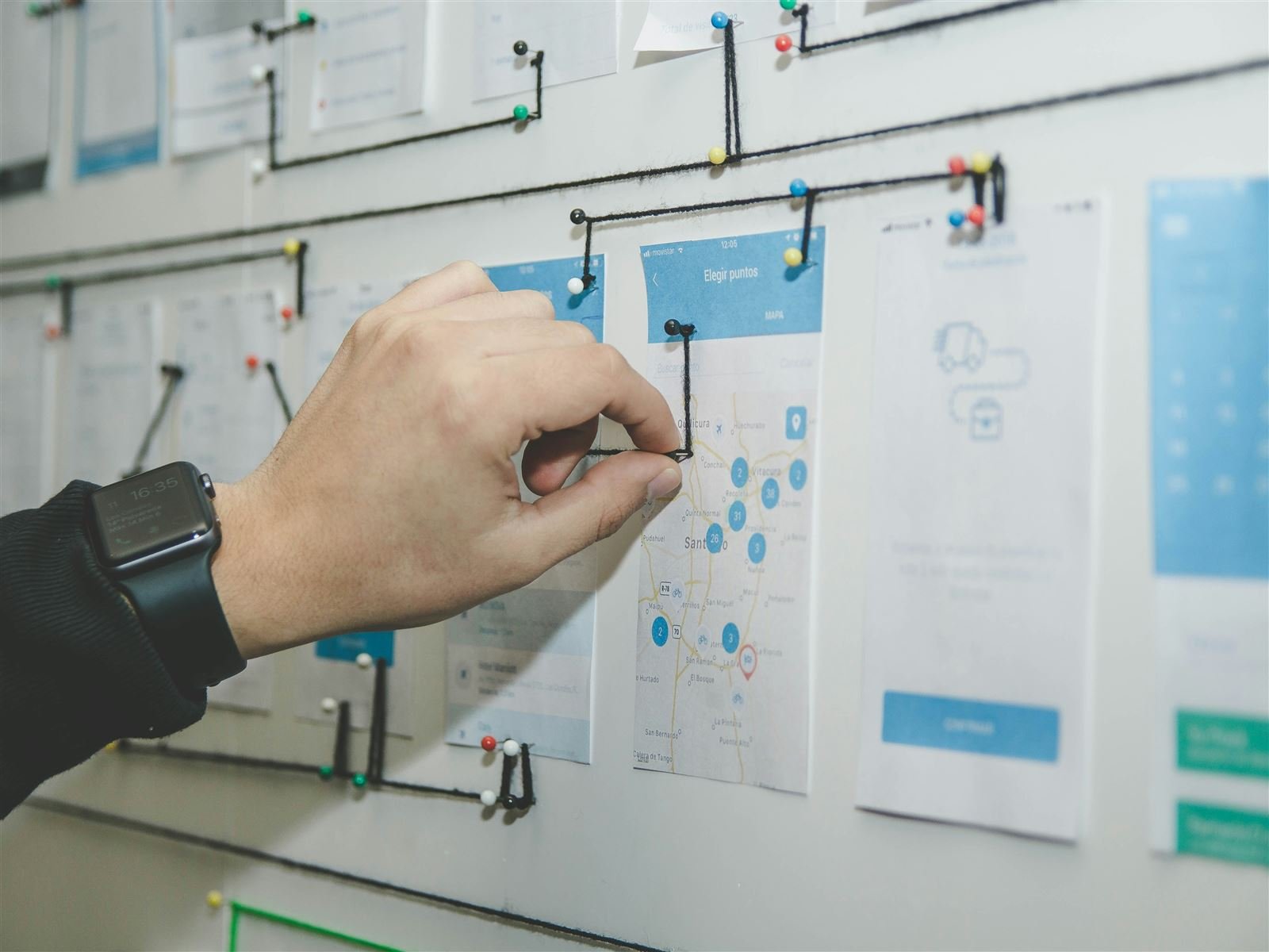 Hand arranging app screen wireframe cards pinned to a wall and connected into a flow