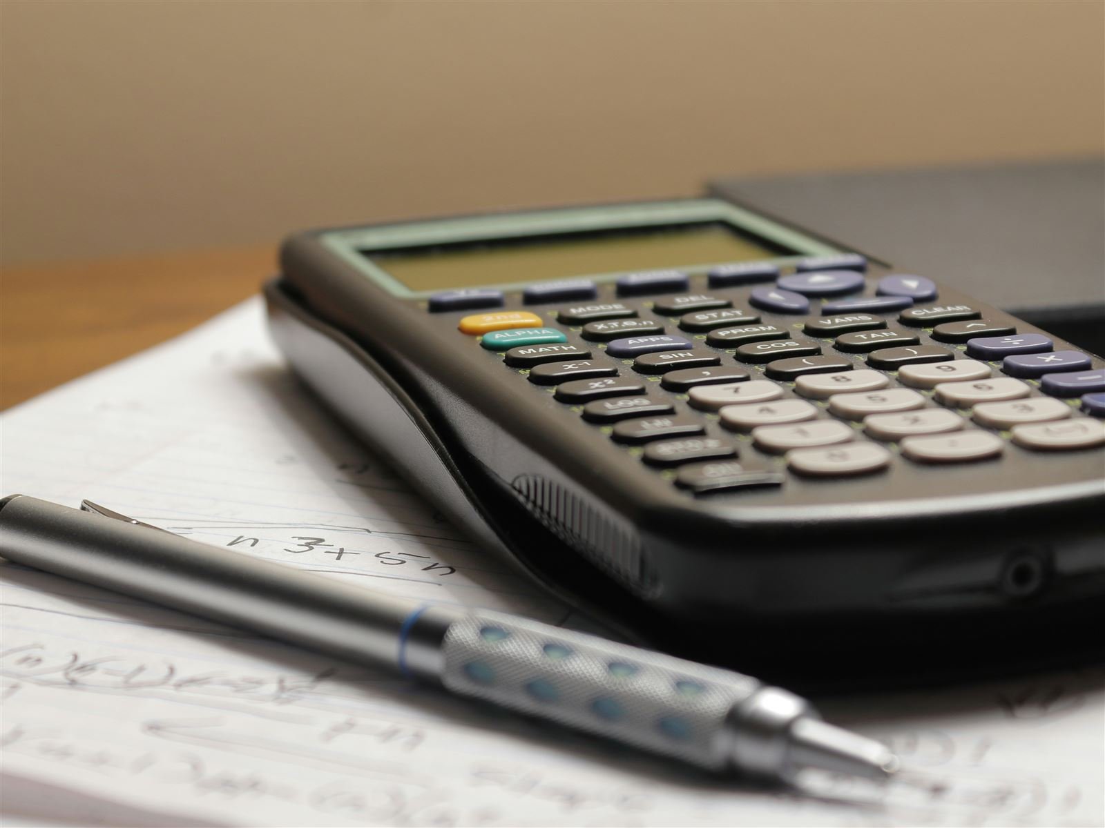 Graphing calculator and a mechanical pencil resting on a page of handwritten calculations